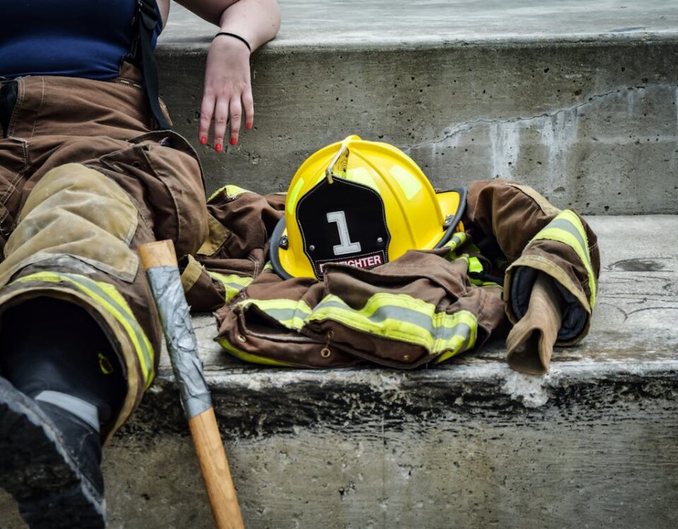 Uniforme NR10: O que a Legislação Diz Firewoman taking a break on concrete steps with gear and helmet nearby.