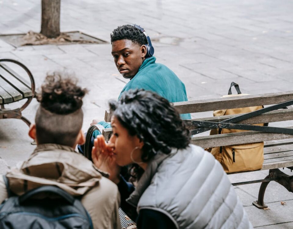 Direitos de resposta em casos de difamação pública Back view of faceless classmates spreading gossip about African American man on wooden bench