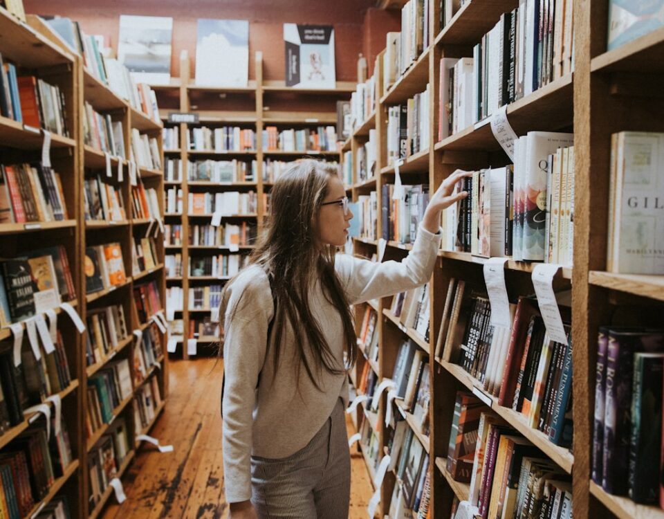 woman holding book on bookshelves