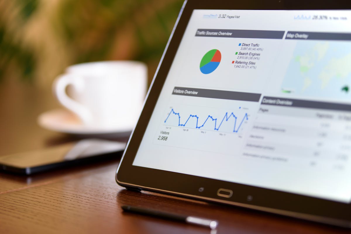 Close-up of a tablet displaying analytics charts on a wooden office desk, alongside a smartphone and coffee cup.