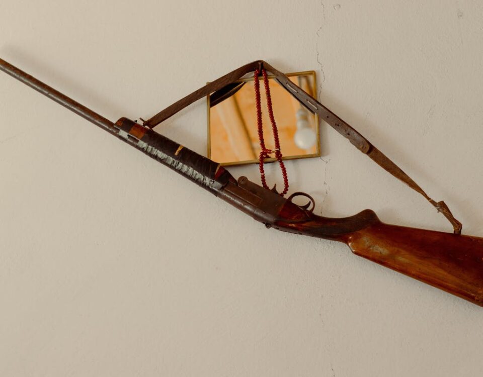 Quais são as leis para posse de espingardas e carabinas? Antique rifle hanging on a wall, complemented by a small mirror reflection.