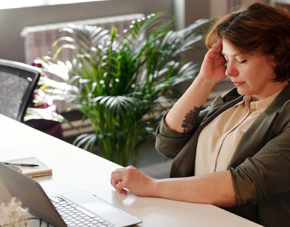 Direitos de pacientes com doenças inflamatórias no trabalho A businesswoman feeling stressed at her home office desk while working on her laptop.