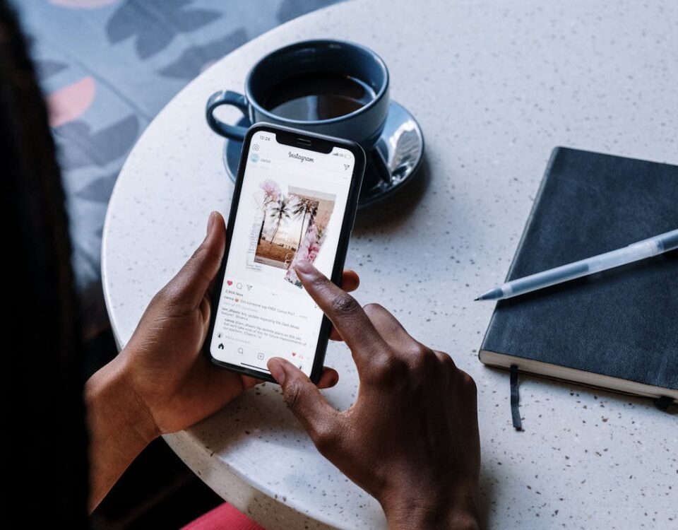 Influência digital e direitos autorais no Instagram Hands holding smartphone at a cafe table with coffee and a notebook, focusing on social media browsing.