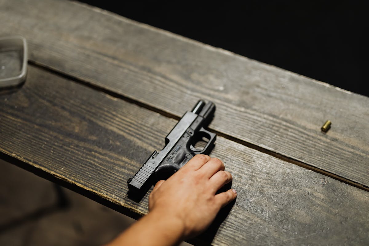 O que diz a lei sobre a posse de armas no Brasil? Close-up of a hand holding a handgun on a wooden table with bullet casing.