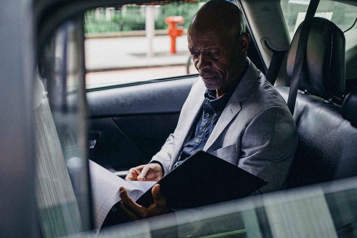 Direitos e deveres ao contratar um seguro de carro Side view serious African American businessman in formal clothes sitting in car back seat and reading documents