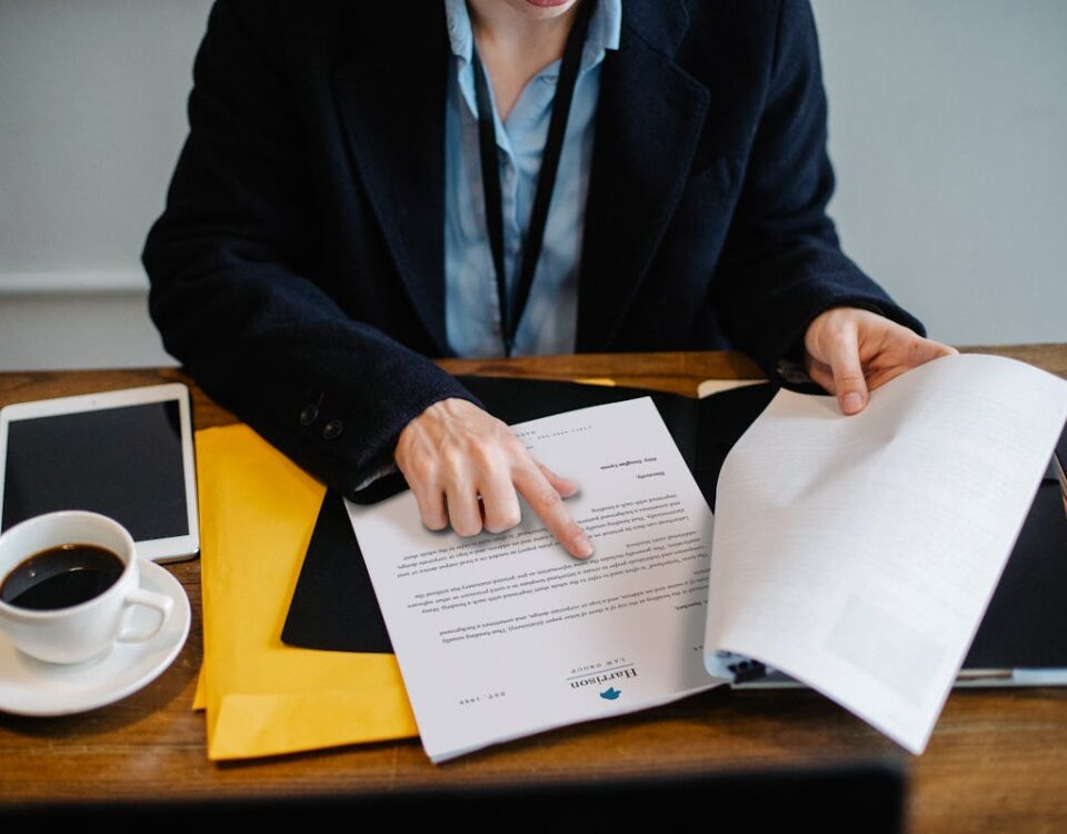 Entenda o processo de obtenção de licença ambiental High angle of crop faceless woman in formal wear sitting at wooden table with tablet and coffee and reading documents