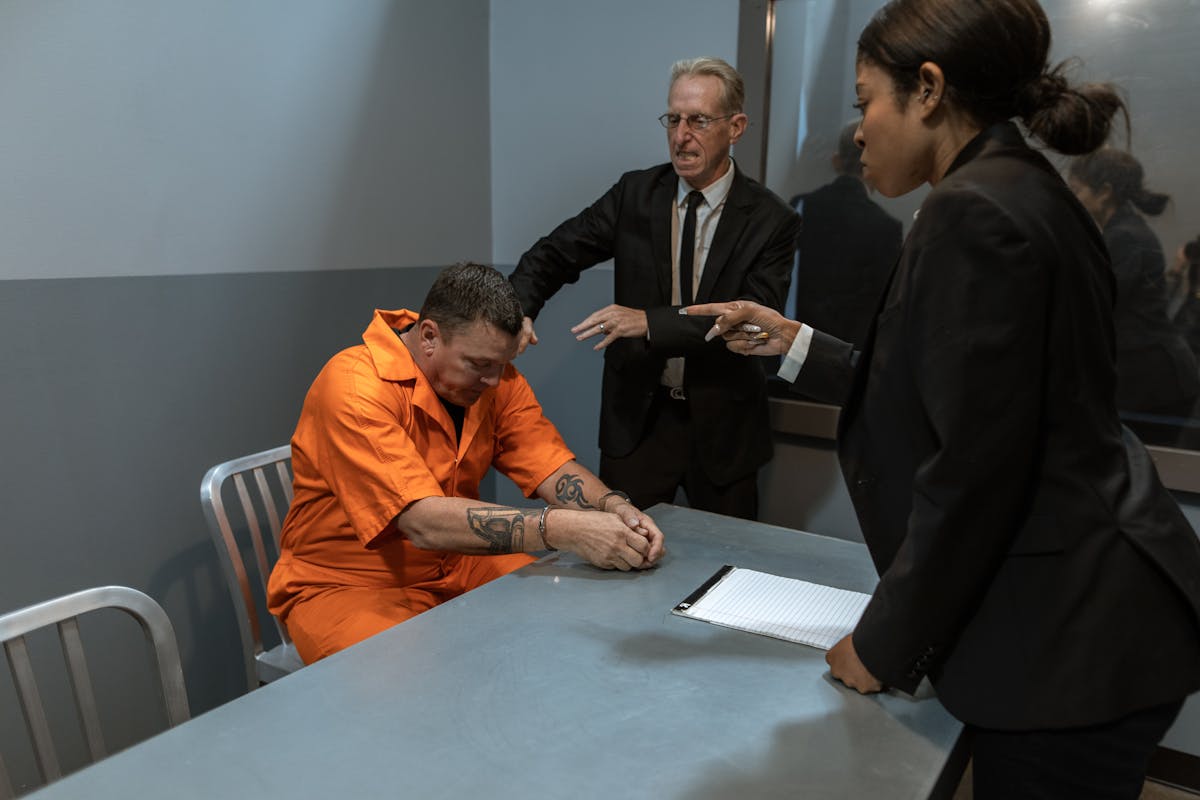 A tense interrogation scene with officers and a prisoner in an orange jumpsuit.