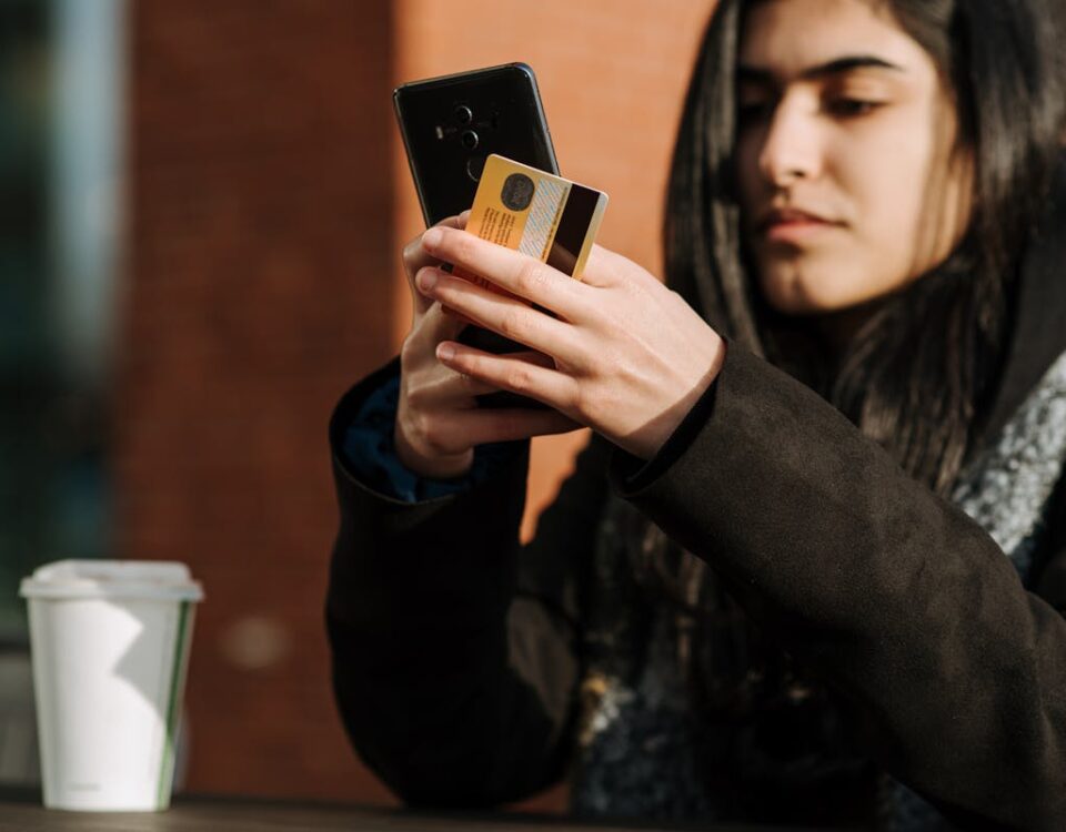 Fatores legais que podem impedir seu cartão de crédito Crop young Hispanic female shopper with debit card making purchase on cellphone near takeaway beverage in cafeteria