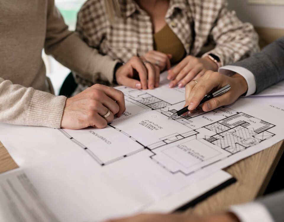 Contratos imobiliários: erros que podem custar caro Group examining house floor plans with a real estate agent, highlighting home buying process.