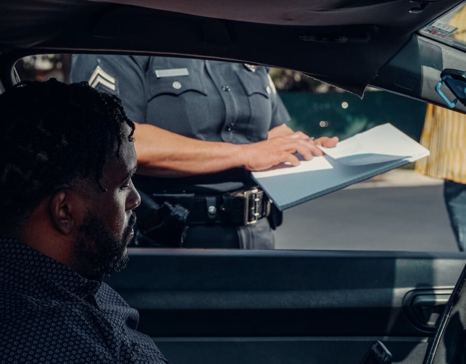 A police officer issues a traffic ticket to a man in a car. Close-up view of the interaction through the window.
