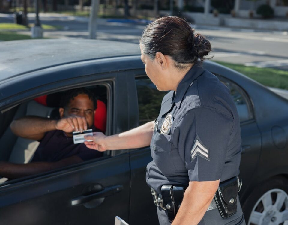 Quais infrações podem suspender sua CNH? A police officer hands a ticket to a driver in a car on a sunny day street.