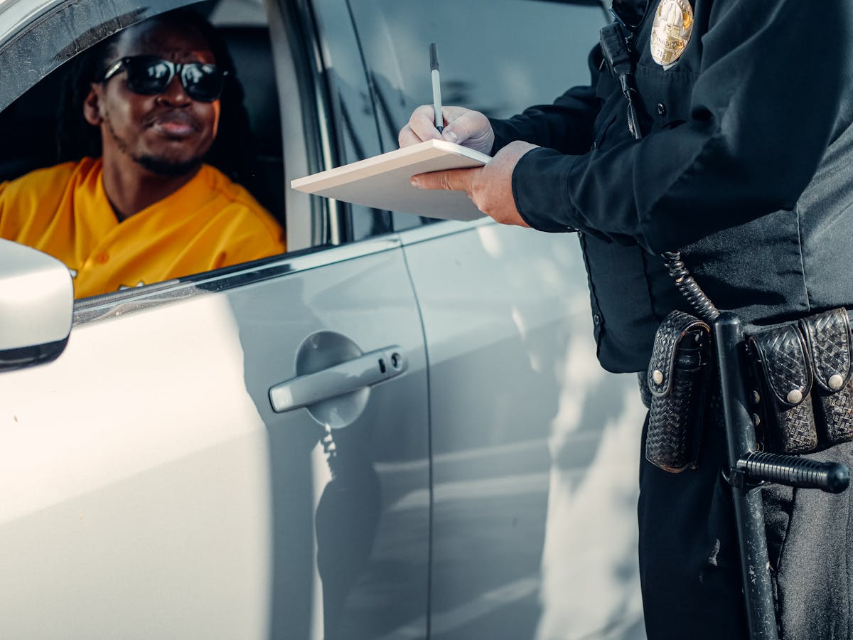 O que fazer se sua CNH for suspensa? A police officer writes a ticket for a driver in a car during a roadside stop.