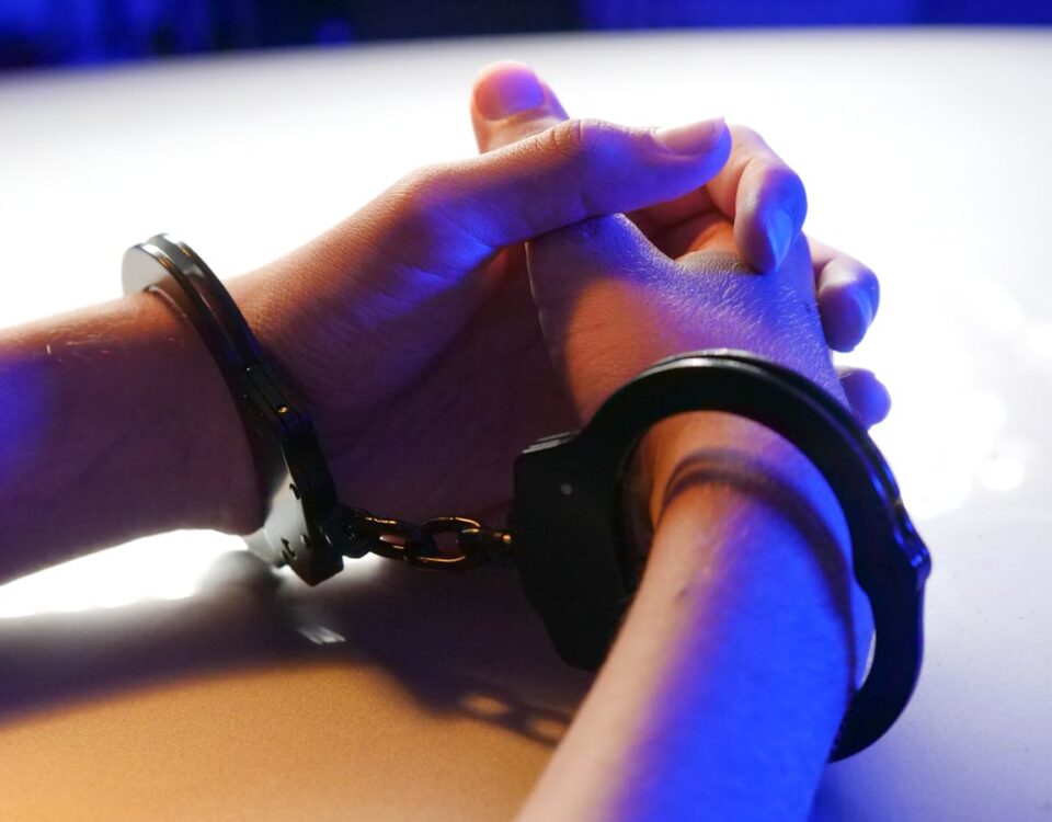Direito ao silêncio: o que você precisa saber sobre esse recurso Close-up of handcuffed hands under blue police light, signifying arrest or detention.