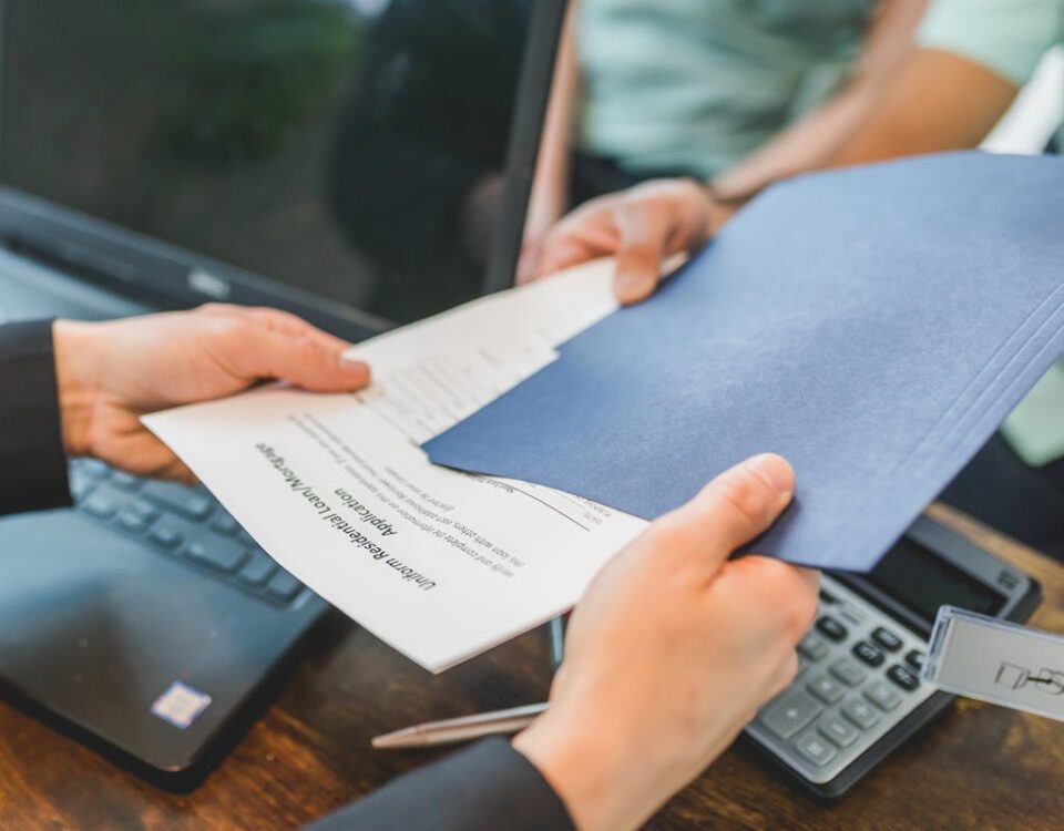 Como evitar fraudes na compra de imóveis? Close-up of hands exchanging real estate documents in an office setting.
