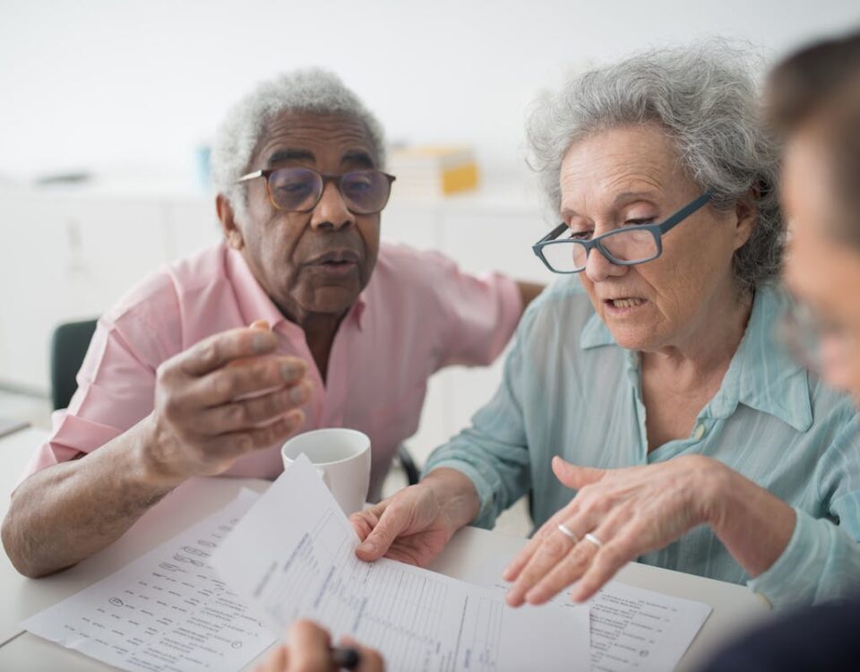 Direitos do consumidor em planos de saúde e seguros Elderly couple discussing financial documents with a consultant in an office setting.