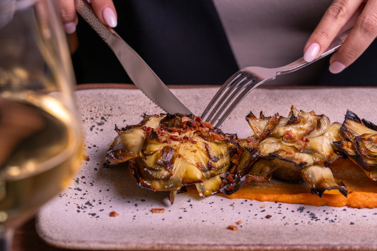 Close-up of a gourmet roasted artichoke being sliced on a plate, perfect for culinary enthusiasts.