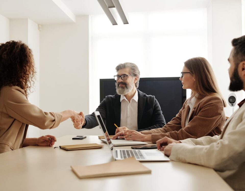 Contratos essenciais para empresas de TI evitarem problemas Colleagues in an office celebrating a successful negotiation with a handshake.