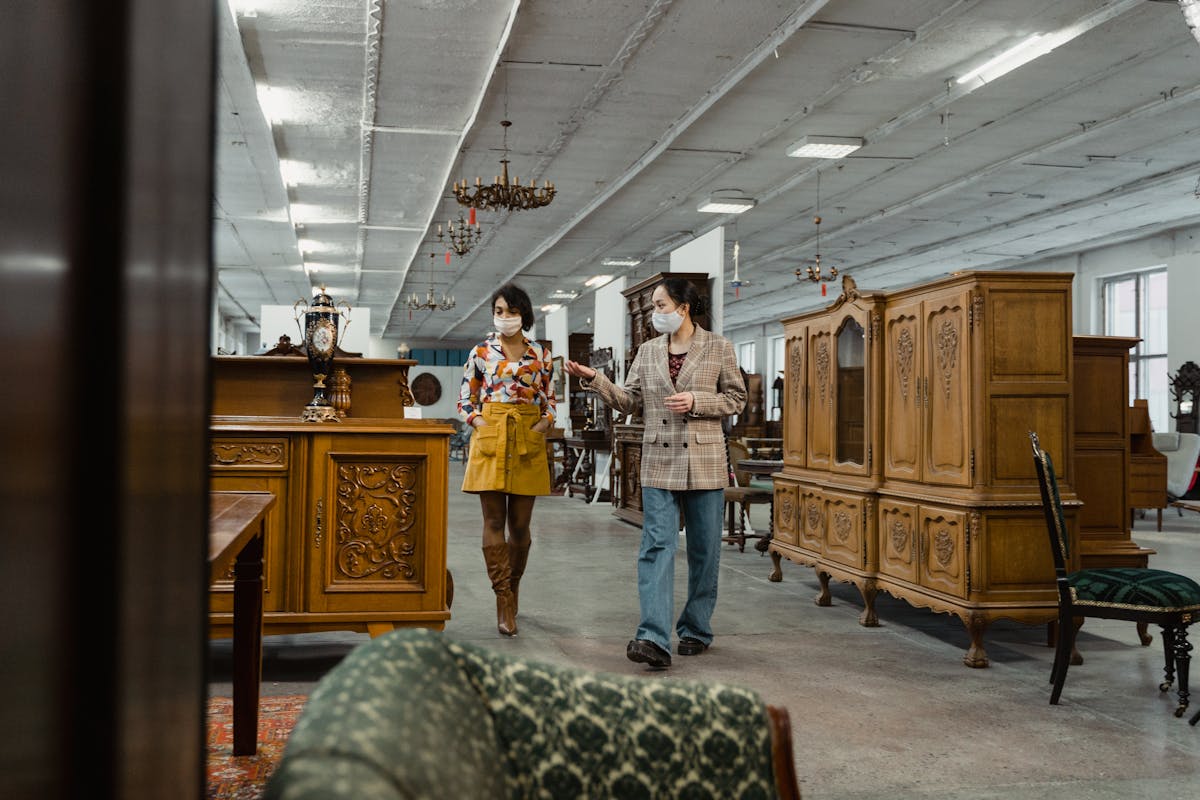 Two adults in masks browse antique furniture in a stylish vintage store.