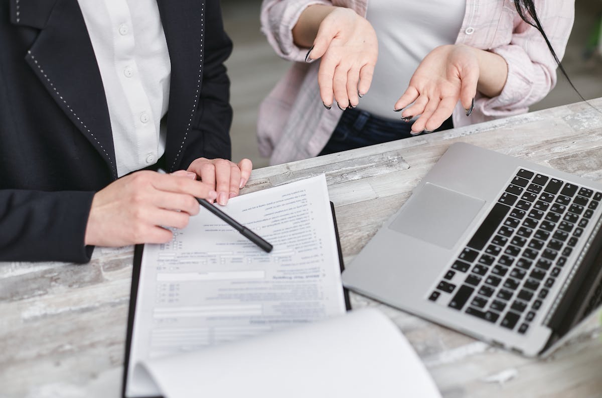 Gestão de arenas e contratos: O que saber? Two professionals discussing a contract at a business meeting with documents and a laptop.