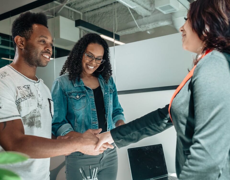 Gestão de arenas e contratos: O que saber? Smiling couple shaking hands with advisor in modern office.