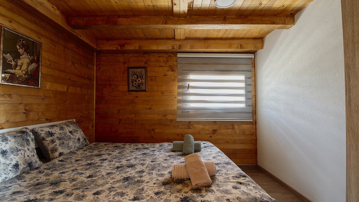 Quarto com paredes de madeira, cama de casal arrumada e toalhas dobradas