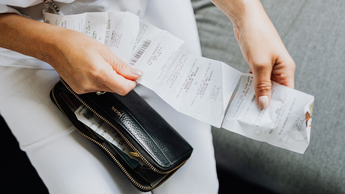 Mãos de uma mulher conferindo notas fiscais de compras ao lado de uma carteira