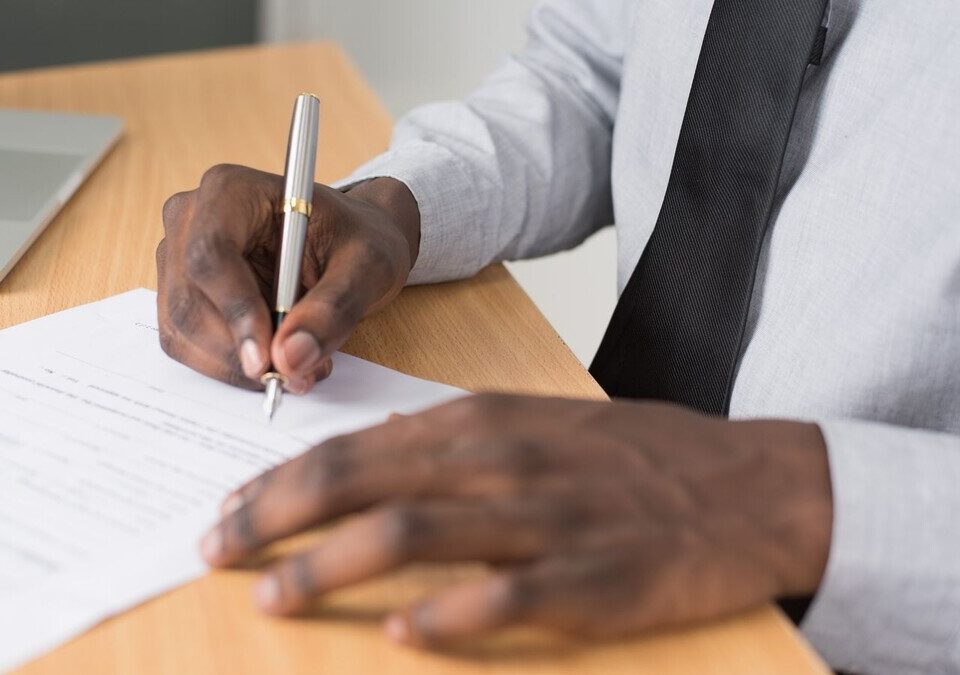 Pessoa assinando um documento sobre uma mesa de escritório