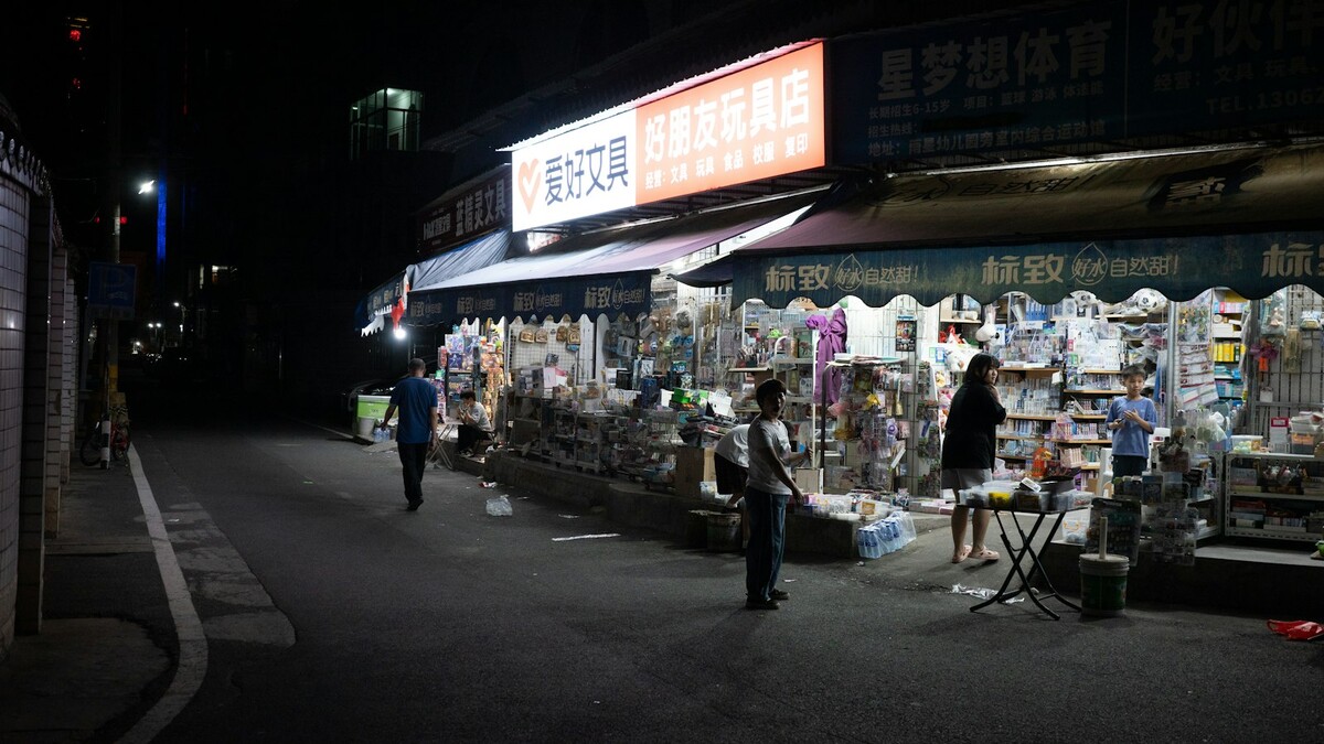 Rua comercial à noite com várias lojas abertas e letreiros acesos