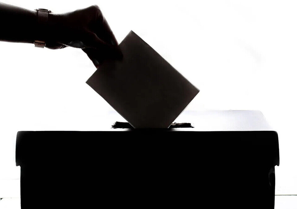 Mão depositando cédula de votação em urna