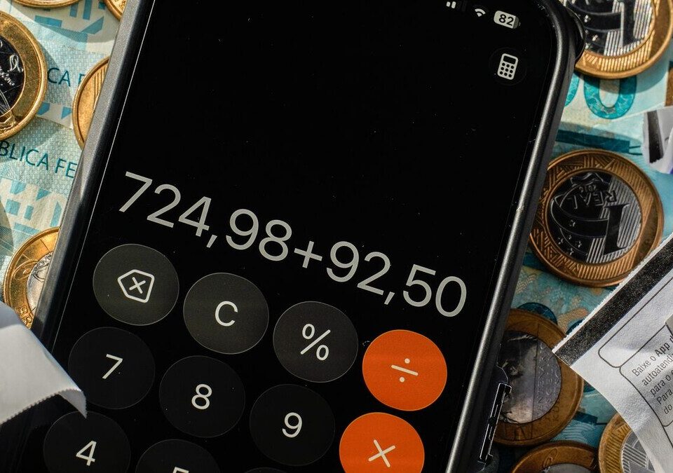 Simples Nacional e reforma tributária: prazo do IBS e CBS acaba em 30/10 Calculadora no celular sobre moedas de real e notas fiscais