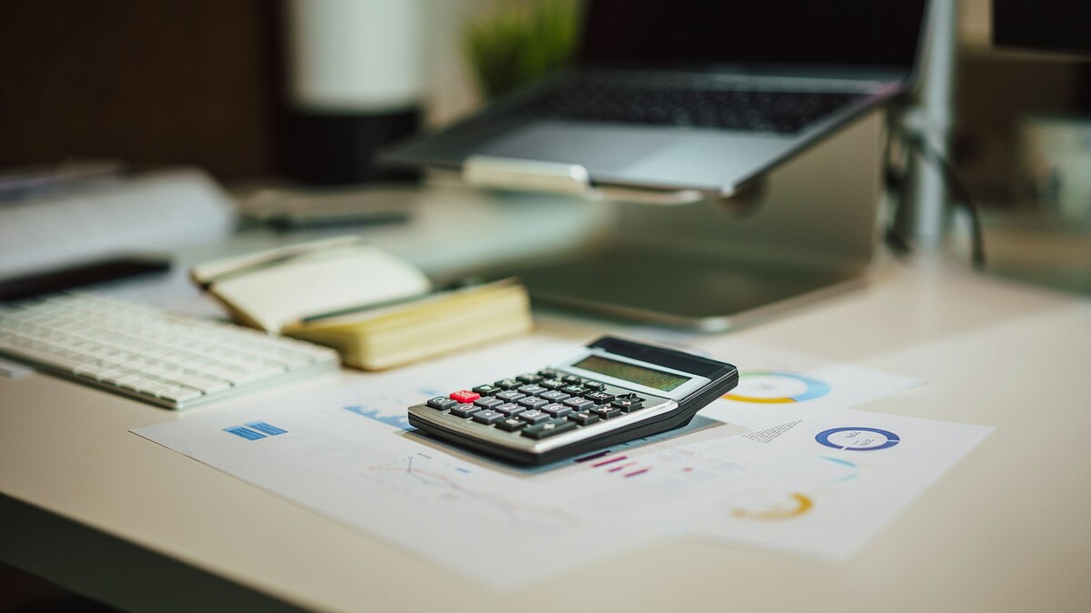 Calculadora sobre uma mesa ao lado de um notebook e papéis